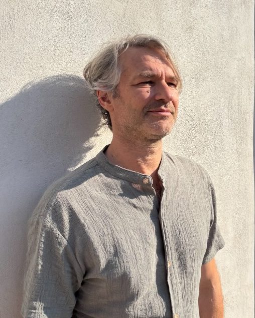 Xavier Herman, debout contre un mur ensoleillé